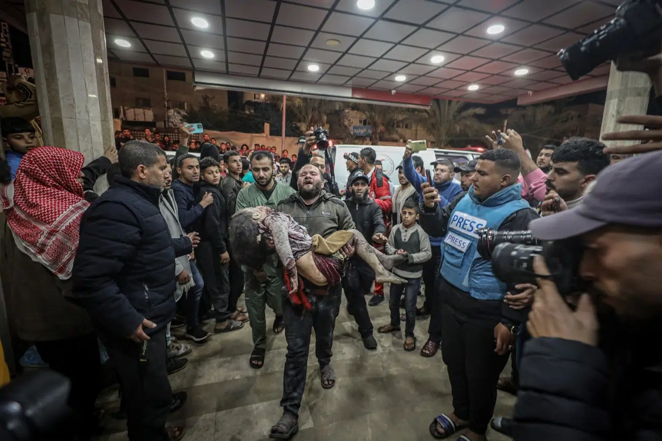 At Nasser Medical Complex, a father rushes in shock, carrying his lifeless daughter, torn apart by an Israeli airstrike.